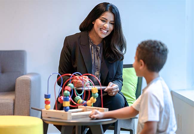Young woman smiling as she watches a child play with a toy.